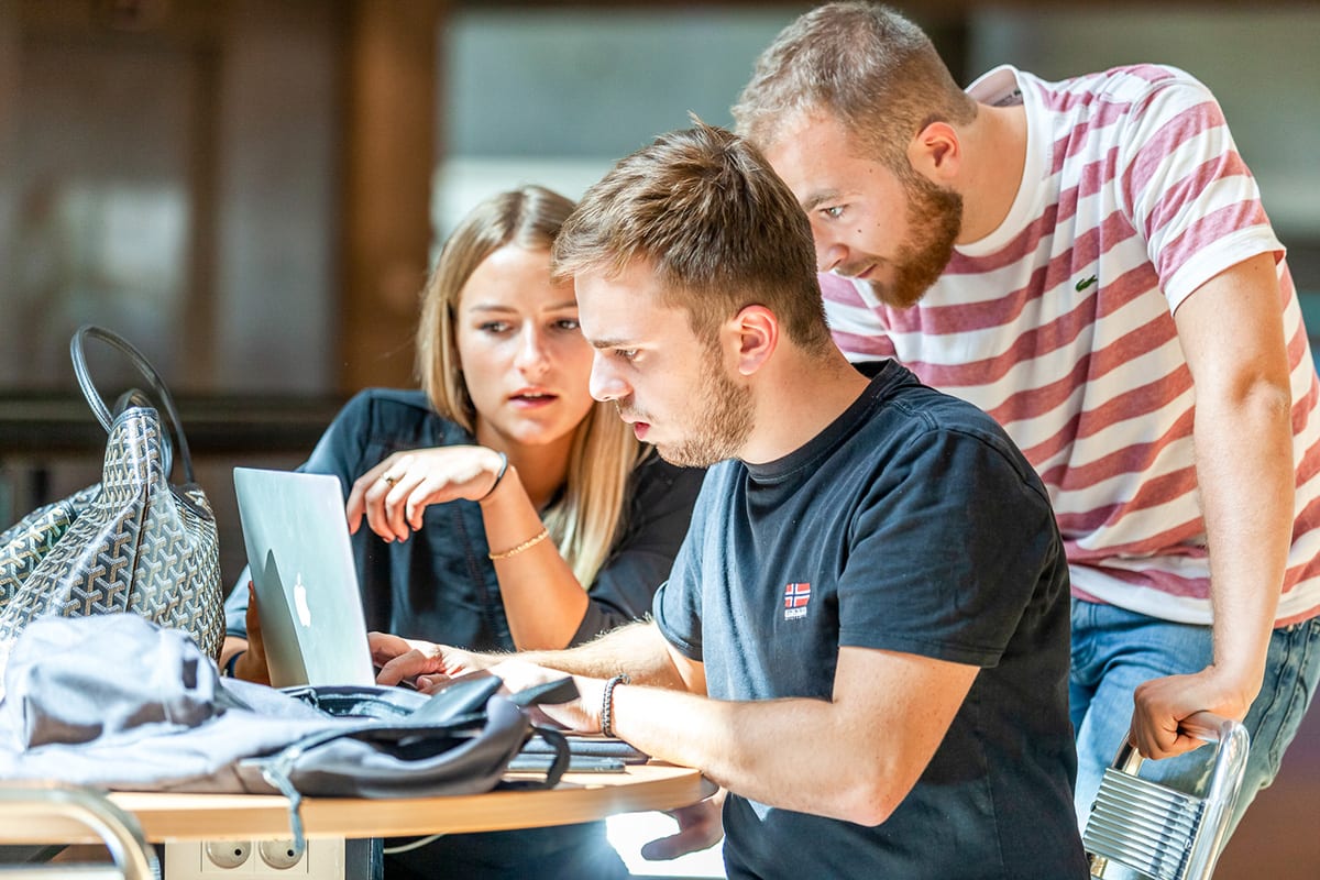 Trois étudiants discutent et regardent un ordinateur portable